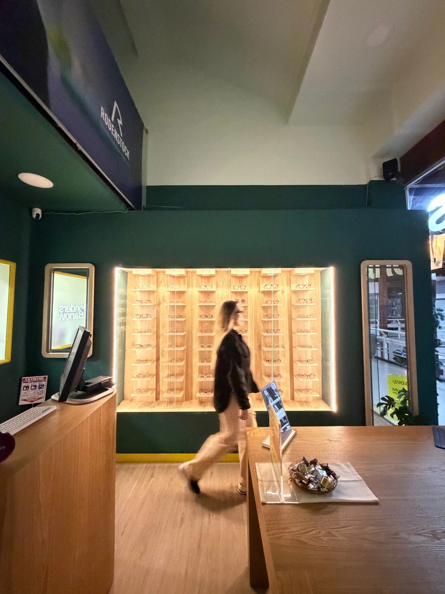 Interior de la tienda: estantería retroiluminada y mesa de madera